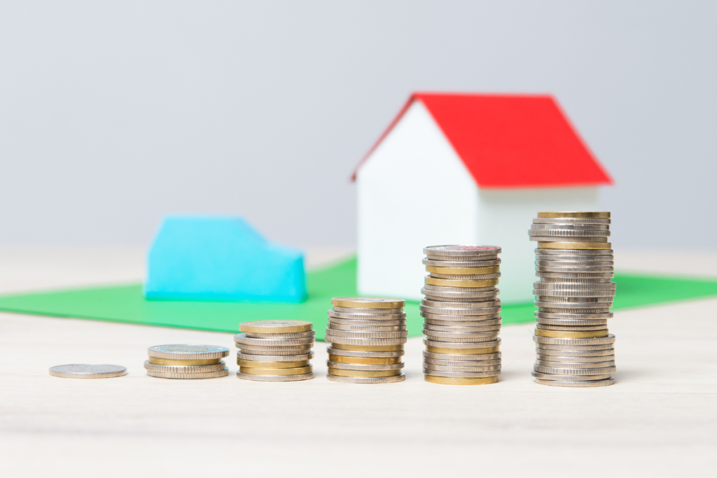 a pile of coins infront of a cardboard house and car