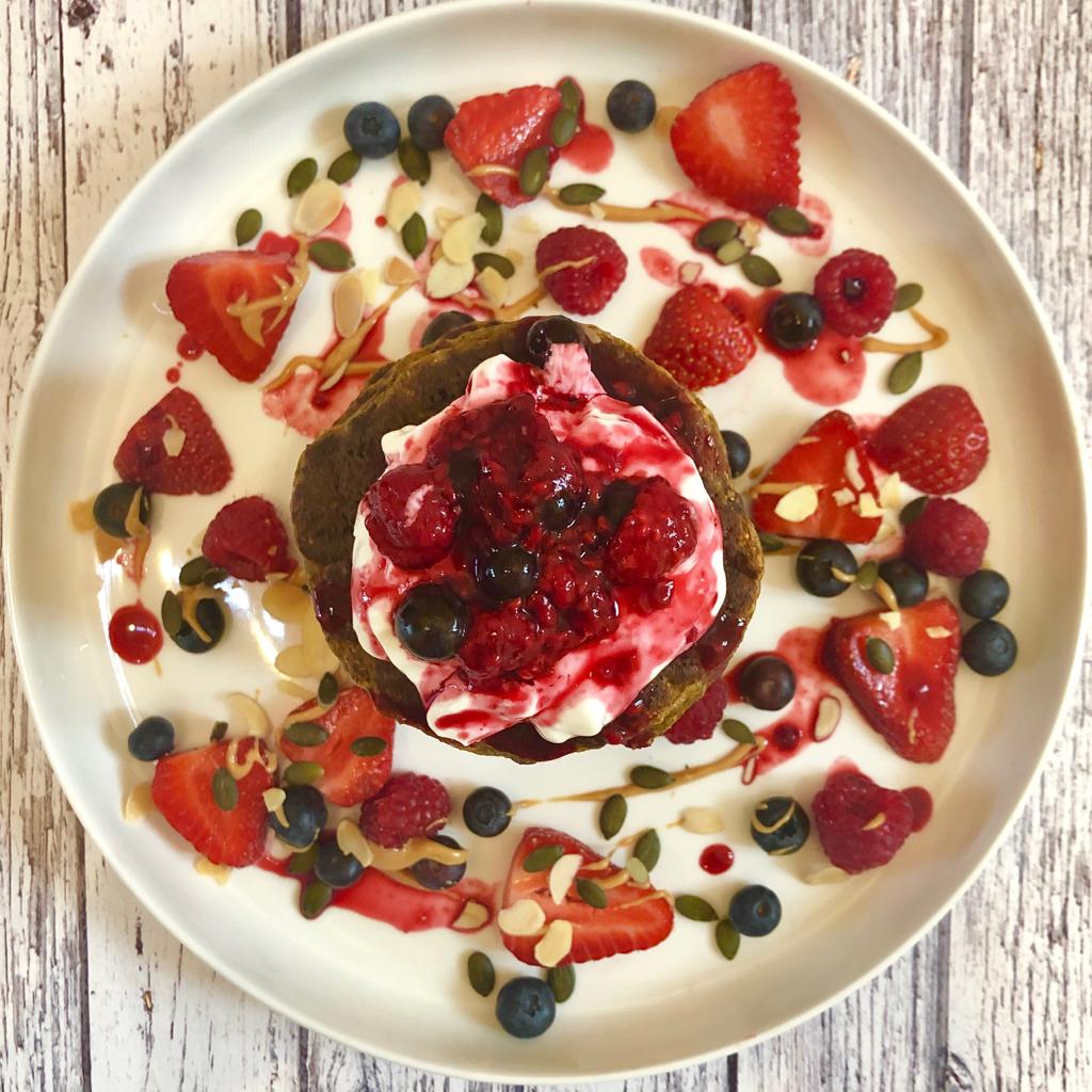 Overhead view of a stack of carrot cake pancakes on a plate topped with yoghurt, a variety of berries and nut butter