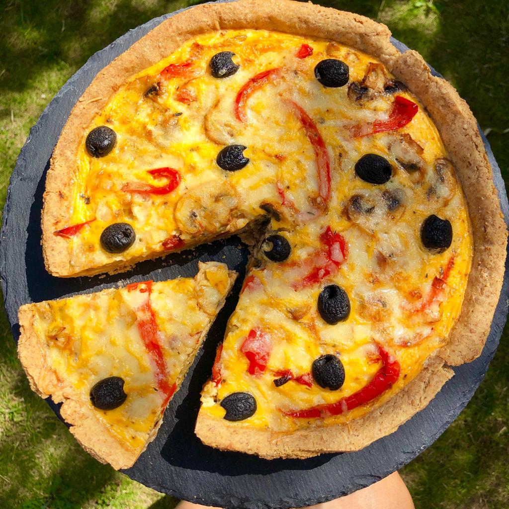 Veggie quiche with a single slice cut, served on a slate chopping board