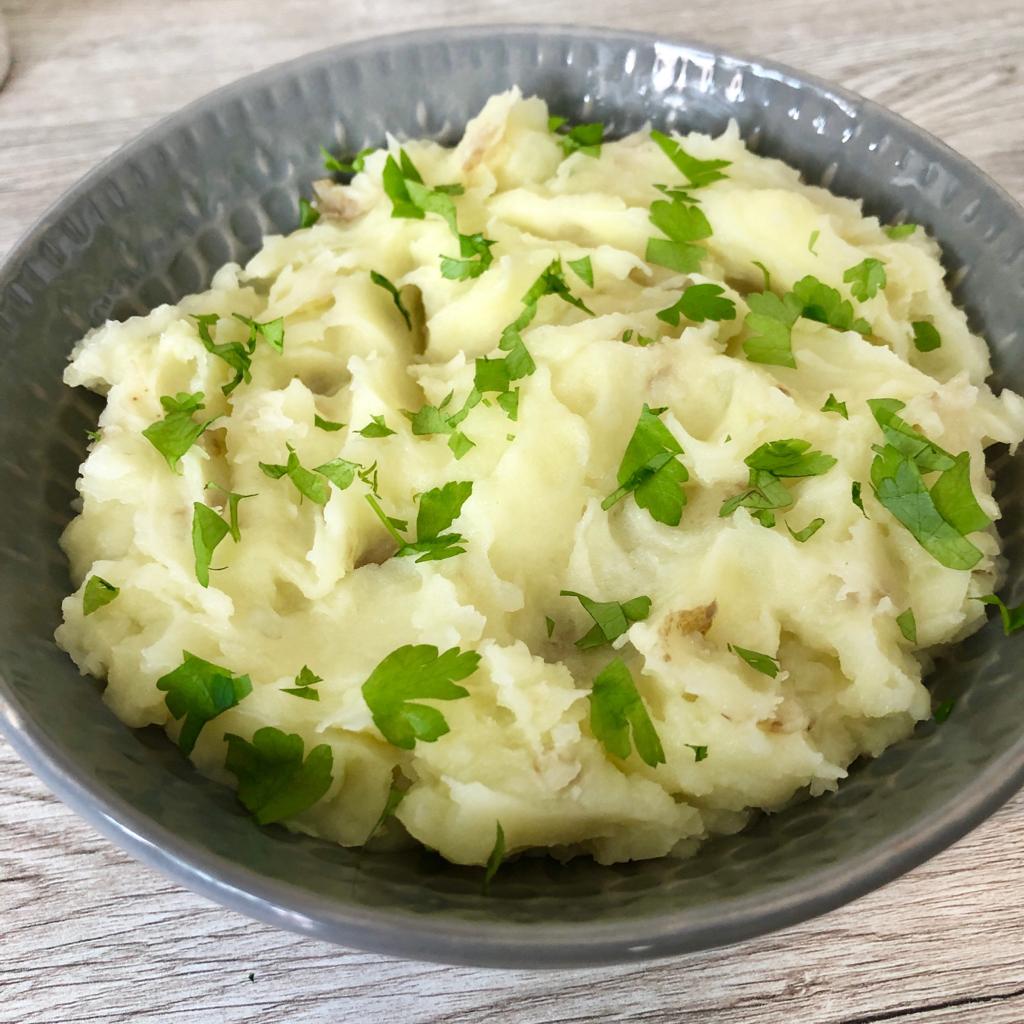 Olive oil mashed potato in a bowl topped with chopped fresh parsley