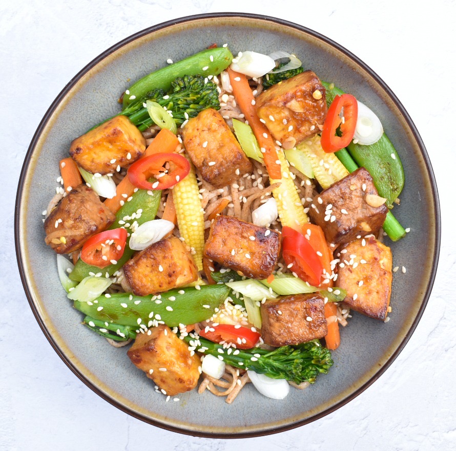 Tofu and vegetable stir fry served in a bowl with noodles and topped with sesame seeds