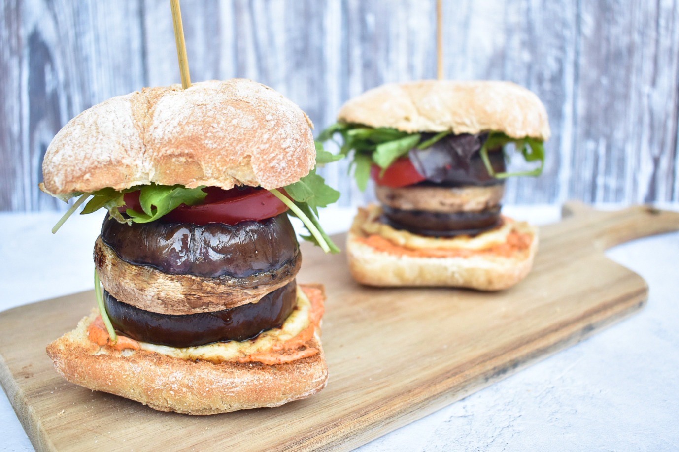 Veggie aubergine burgers with skewers through them, served on a wooden chopping board