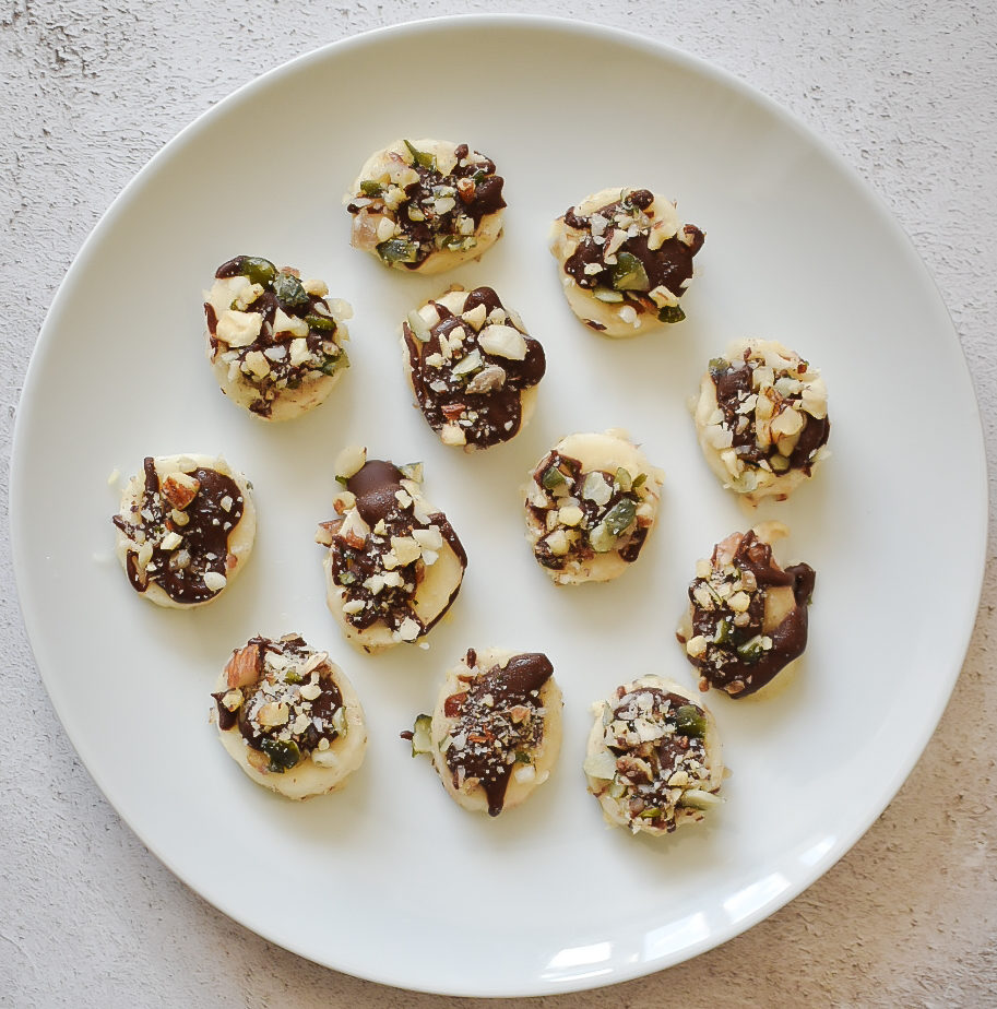 Plate of frozen banana slices topped with chocolate and chopped nuts