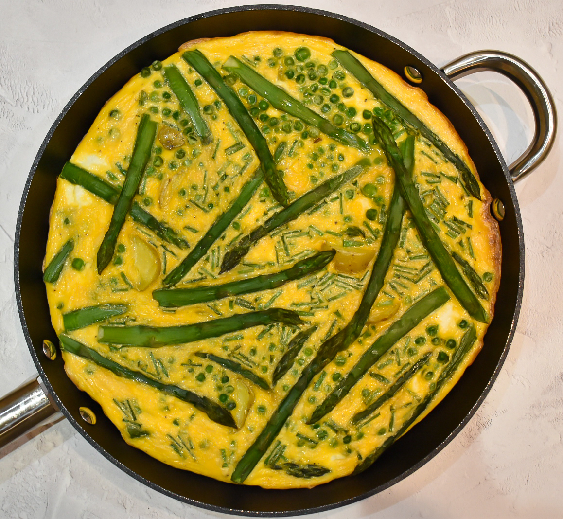 Asparagus, pea, new potato and ricotta frittata in a frying pan