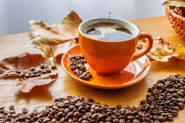 an orange coffe cup surrounded my autumn leaves and coffee beans