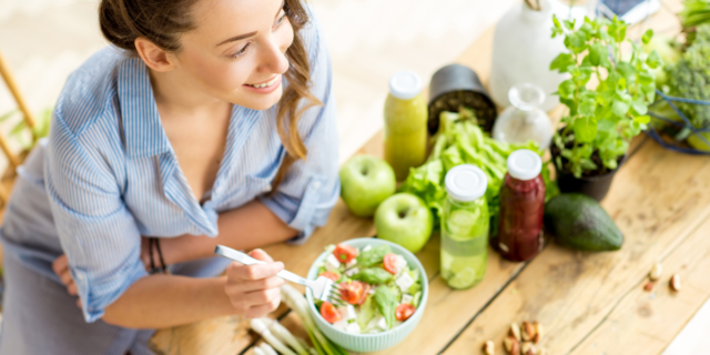 young woman eating a salad surrounded by fruit and vegetables