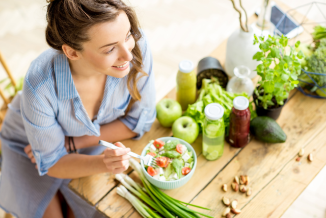 5 young woman eating a salad surrounded by fruit and vegetables