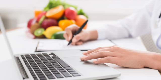 a woman working on a laptop with a pile of fruit in the background