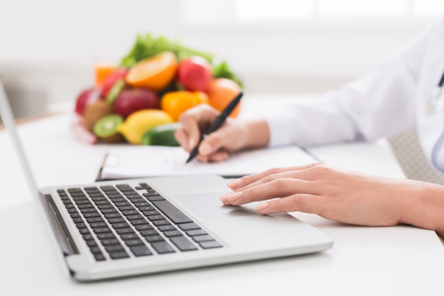 Untitled design (47) a woman working on a laptop with a pile of fruit in the background