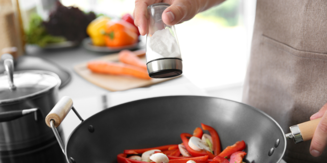person adding salt whilst cooking a meal
