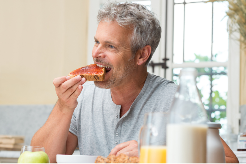 mature man eating a slice of toast and jam for breakfast