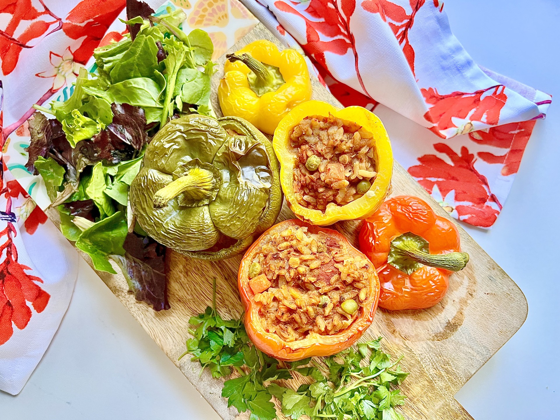 A wooden serving platter with one red pearl barley and lentil stuffed pepper and one yellow pearl barley and lentil stuffed pepper and one green pearl barley and lentil stuffed pepper