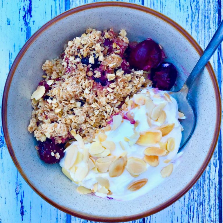 Bowl of cherry and almond breakfast crumble with Greek yoghurt and toasted almonds
