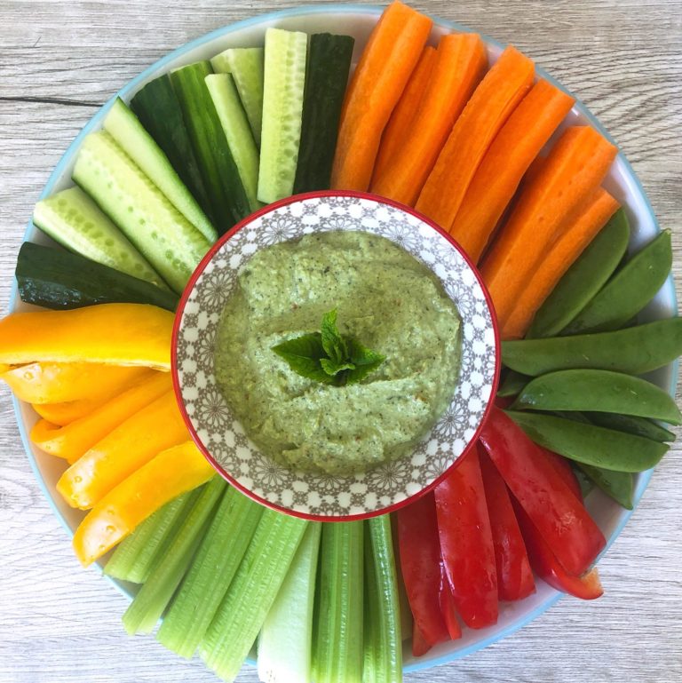 Edamame bean and mint dip in a bowl topped with fresh mint leaves, surrounded by a variety of vegetable sticks