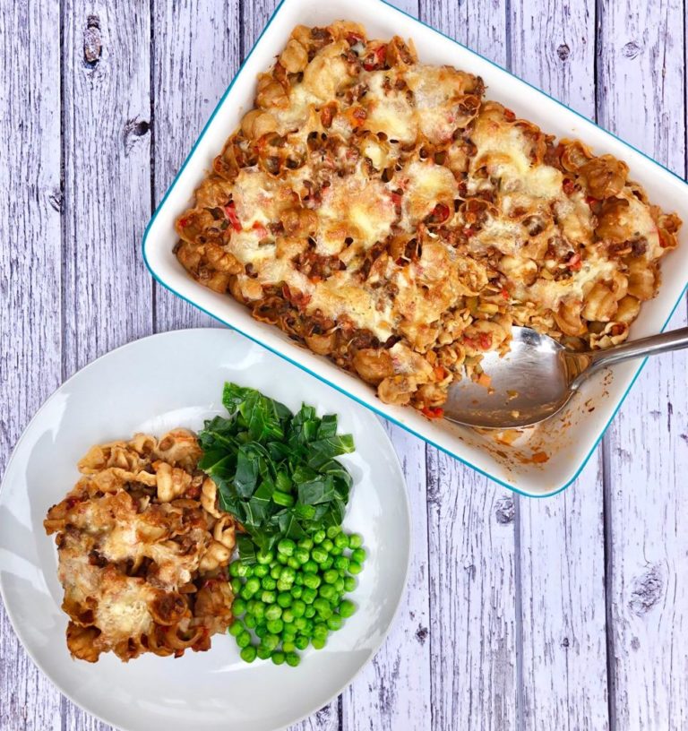 Bolognese bake with a missing portion, alongside a plated serving with peas and steamed greens