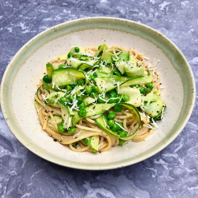 Pea and courgette carbonara in a bowl topped with black pepper and grated parmesan